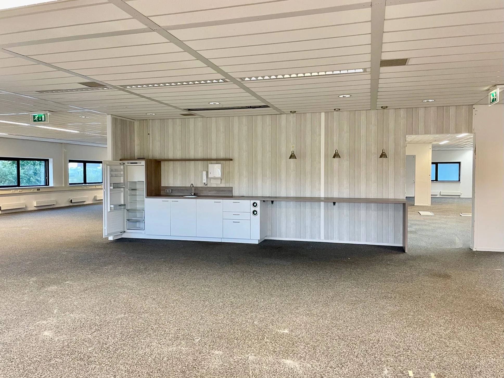 Open kantoorruimte aan de Karel Doormanweg met ingebouwde pantry en grijze vloerbedekking.